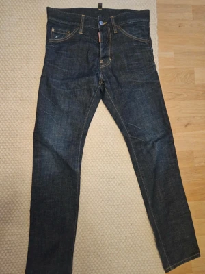 Dsquraed2 jeans mörkblå jeans straight fit - Klassiska dsquared2 jeans i mörkblå denim med raka ben och fem fickor. Jeansen har gul kontrastsöm, knappgylf och den ikoniska röda Levi's-lappen vid fickan. Perfekta för dig som gillar tidlös och clean stil.