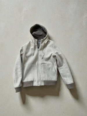 Beige hoodie med dragkedja från Dan John  - Snygg beige hoodie med dragkedja framtill från Dan John/ italien och stora fickor. Huva med dragsko och kontrastfärgad insida i grått. Ribbstickade muddar vid ärmslut och nederkant ger en schysst look. Perfekt för en avslappnad stil. Denna hoodie är inte som alla andra gjord i Rom 🇮🇹har en innesida som håller dig varm så fungerar utmärkt som tunnare jacka och att ha inne! 