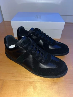 Svarta sneakers från Maison Margiela - 🛑Stilrena svarta sneakers från Maison Margiela i skinn och mocka. Klassisk låg modell, snörning och svart yttersula.🛑 Knappt använda, nyskick. 🛑Kom gärna med frågor eller funderingar som t.ex. fler bilder. 🛑Snabb affär= diskutera priset!!!