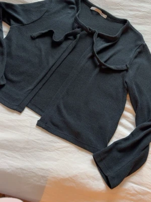 Mörkblå stickad kofta med knytband - Mysig mörkblå stickad kofta med långa ärmar och knytband vid halsen. Koftan har en avslappnad passform och är tillverkad i ett mjukt, tunt stickat material. Enkel att styla till olika outfits.