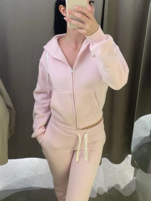 Ljusrosa mjukisdress med dragkedja - Supermysig ljusrosa loungewear-set med hoodie och matchande byxor. Hoodien har dragkedja, fickor och snörning i huvan. Byxorna har resår i midjan och vita snören. Perfekt för chill dagar hemma.