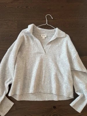 Ljusgrå stickad tröja från Monki - Mysig ljusgrå stickad tröja från Monki med krage och v-ringad hals. Tröjan har avslappnad passform, ribbade muddar och nederkant. Perfekt för lager på lager och enkel att styla till olika outfits.