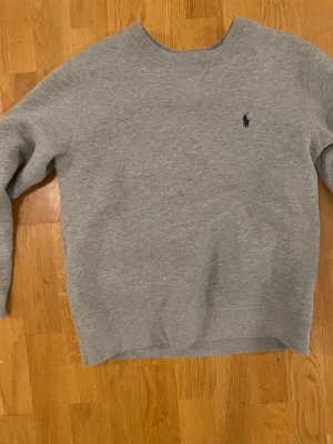 Ralph Lauren crewneck - En grå Ralph Lauren crewneck i storlek junior large , använd sparsamt i ungiefär ett halv år . Skick 9/10 om inte bättre . Inge defekter 