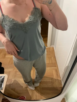 Ljusgrå linnetopp med spetsdetaljer - Supersöt ljusgrå linnetopp med tunna axelband och vacker spets längs v-ringningen. Toppen har en avslappnad passform och är perfekt för mysiga hemmadagar. Materialet känns mjukt och lätt mot huden.