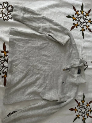 Ljusgrå långärmad tröja Polo Ralph Lauren - Ljusgrå långärmad tröja från Polo Ralph Lauren med liten broderad logga på bröstet. Tröjan har half zip-dragkedja vid halsen och är tillverkad i mjuk bomull. Perfekt för en avslappnad och stilren look.