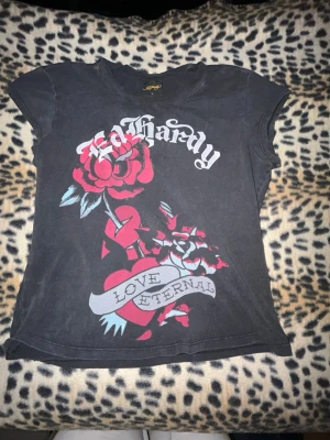  Ed Hardy t-shirt - Säljer en svart t-shirt från Ed Hardy med stort färgglatt tryck av ros och hjärta på framsidan samt texten 'Love Eternal'. T-shirten har korta ärmar och en normal passform. L i barnstorlek men passar mig som är S-XS