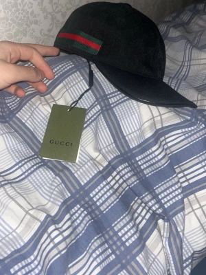 Keps - En snygg svart keps med en ikonsk röd gröna ränder på sidan med gg märken på. Justerbart rem där bak för en perfekt passform med lappar på