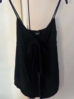 Svart linnetopp med knyt framtill - Svart linnetopp från Gina Tricot med tunna axelband och knyt framtill. Oanvänd 