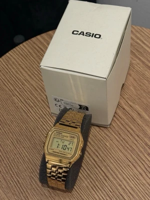 Guldfärgad digital klocka Casio - Stilren digital klocka från Casio i guldfärgad metall med klassisk länkarmband och rektangulär display. Klockan har digital tidvisning, datum och alarmfunktion. Perfekt accessoar för dig som gillar retrostil och vill ha något som sticker ut.