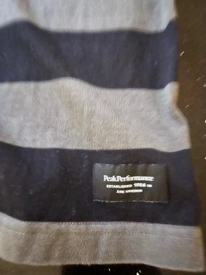 Randig Peak Performance skjorta - Snygg långärmad skjorta från Peak Performance med breda svarta och gråa ränder. Klassisk krage och knappar framtill. Tillverkad i mjuk bomull som känns skön mot huden. Perfekt för en avslappnad men ändå stilren look.