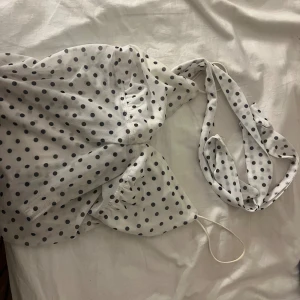 Eftertraktad prickig Zara topp  - Säljer en vit eftertraktad Zara topp med svarta prickar och omlott-design. Toppen har tunna axelband och en snygg v-ringad urringning. Materialet känns lätt och passar perfekt för varma dagar. Prickigt mönster ger en cool retrovibe och den sitter snyggt med figurnära passform. Osäker på om S eller Xs men passar båda.