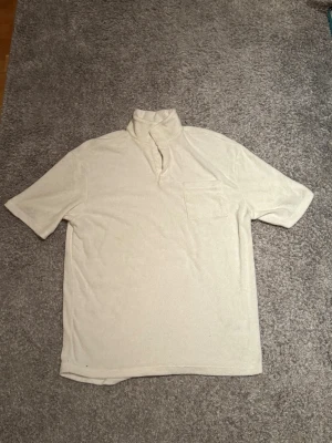 Vit pikétröja i frotté - Vit pikétröja i mjukt frottématerial med kort ärm, hög krage och bröstficka. Skön och luftig med en stilren, vintage-inspirerad look. Perfekt till sommaren eller avslappnade outfits.  🟢 Skick: Bra skick 🟢 Storlek: Herr S 🟢 Färg: Vit 🟢 Material: Frotté  Hör av dig om du vill ha fler bilder eller mått 📩