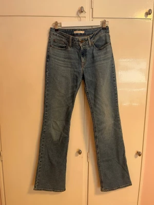 Levi's jeans  - Klassiska blå Levi's  jeans med bootcut passform. Jeansen har fem fickor, normal midja och ikonisk läderpatch bak i linningen. Tillverkade i slitstarkt denimtyg av bomull. Perfekta för dig som gillar en tidlös och avslappnad look. De är i storleken W27 L34.