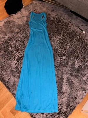 Blå långklänning i bomull - Snygg blå långklänning med ärmlös design och sportigt brottarrygg. Tillverkad i mjuk bomull, perfekt för varma dagar. Enkel och stilren modell som är lätt att matcha med accessoarer.