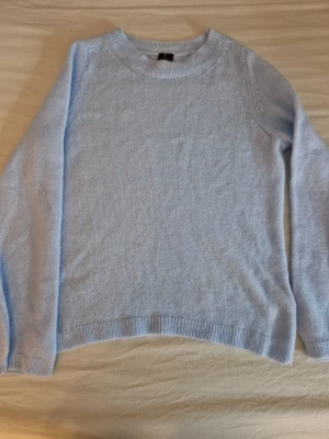 Ljusblå stickad tröja Vero Moda - Mysig ljusblå stickad tröja från Vero Moda med rund halsringning och långa ärmar. Tröjan har ribbade muddar vid ärmslut och nederkant, perfekt för lager på lager under kyliga dagar. Enkel och stilren design som passar till det mesta. Helt oanvända, men Lapparna är bortplockade. Hund finns i hemmet.