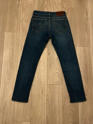 Tiger of Sweden Jeans - Mörkblå Tiger of Sweden jeans med klassisk femficksdesign och raka ben. Jeansen har en snygg tvätt och subtila slitningar framtill. Tillverkade i bomull med en liten mängd stretch för extra komfort. Perfekta för en avslappnad och stilren look. Storlek 30/32