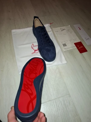 Mörkblå sneakers från Christian Louboutin i storlek 42 - Säljer nu dessa helt nya snygga mörkblå sneakers från Christian Louboutin i mocka med klassisk röd sula och rund tå. Skorna har snörning och stilren design, perfekta för dig som gillar exklusiva detaljer och vill sticka ut med en ikonisk look. Kommer med dustbags, certification card, kontrakt. Priset är självklart diskuterbart. Skorna är i storlek 42 och är helt nya 