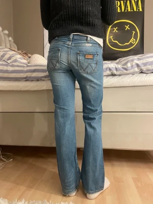 Blå bootcut jeans från Wrangler - Säljer ett par klassiska blå jeans från Wrangler med bootcut passform. Jeansen har fem fickor, snygga sömmar på bakfickorna och lågmidjade. Midjemåttet är 38 cm och innerbenslängden är 79 cm, sitter som en S men lite tajt passform vid rumpa och lår!