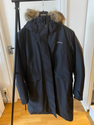 NY varm vinterjacka, Didriksons Parka ”Erika” - Ny snygg svart Didriksons damjacka i storlek 46. Jackan är tillverkad med 100% vattentätt material och har STORMsystem® för skydd mot väder och vind. Den är fodrad och har en huva med avtagbar pälskant. Nyskick, endast använd vid 2 tillfällen vintern 2024-2025. Nypris 3000 kr. Perfekt för kalla dagar med sin långa modell och varma material.