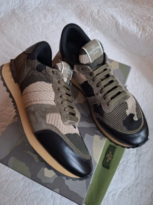 Valentino Rockrunners camo sneakers - Snygga sneakers Rockrunners från Valentino Garavani med camouflage-mönster i grönt, beige och svart. Skorna har snörning, rund tå och detaljer i mocka, mesh och skinn.  Fotlängd ca 28.3 cm Smal passform. Ingår kartong, tygpåse och extra snören. 