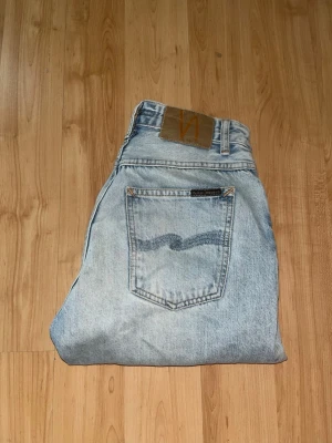 Nudie jeans  - Snygga ljusblåa jeans från nudie jeans. Midja 33cm, längd 98cm. JAG SKICKAR EJ FLER BILDER NÄR JAG BÄR JEANSEN! för bättre inblick i passformen rekommenderar jag att googla på modellnamnet. För storleksguide kolla måtten noggrant då jeansen alltid kan vara uppsydda heller krympta och jag ej tar emot returer :) s6,3