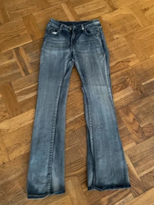 Blå bootcut jeans med slitningar - Snygga blå bootcut jeans med lätt slitning och klassisk femficksdesign. Jeansen har en något utsvängd passform nertill och normal midja. Perfekta för en avslappnad och trendig look. De är i lite stretchigt material.