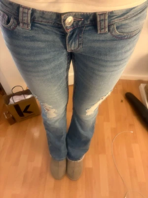 Blå bootcut jeans - Snygga blå bootcut jeans med slitna detaljer på låren och knäna. Jeansen har rosa detaljer. Perfekta för dig som gillar en avslappnad men trendig stil. OBS‼️dem är använda max 3ggr bara men har ett hål i rumpan som går att sy men det är inget jag vet hur man gör så säljer till nån som vet hur man gör de❣️
