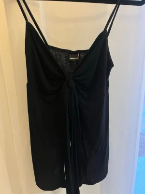 Svart linnetopp med knyt från Gina Tricot - Svart ärmlös linnetopp från Gina Tricot med smala axelband och snygg knytning framtill. Toppen har en lätt v-ringad form.