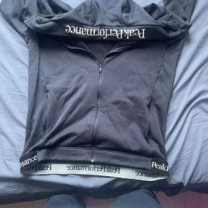 Svart fleecehoodie Peak Performance M - mörkblå hoodie från Peak Performance i fleece med hel dragkedja och huva. Snygg logga på huvkanten och nederkanten. Perfekt för kyliga dagar och outdoor-aktiviteter. Mjuk insida och sportig look.