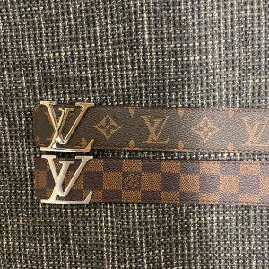 Louis Vuitton bälte monogram & rutig - Två snygga Louis Vuitton bälten i klassisk design. Ena bältet har det ikoniska monogrammönstret i brunt och beige, det andra har rutigt Damier-mönster i mörkbrunt och brunt. Båda har en silverfärgad LV-spänne och är tillverkade i skinn. Perfekt accessoar för att lyfta din outfit.