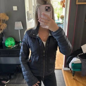 Svart pufferjacka - Säljer en svart pufferjacka från parajumper med broderad patch på ärmen. Jackan har dragkedja framtill, hög krage och två fickor med dragkedja. Perfekt för kyliga dagar och har en snygg, figurnära passform.