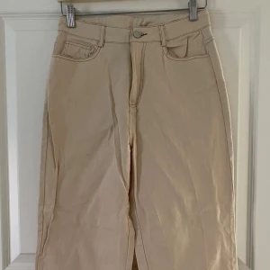 Beiga raka byxor från DAZY, M - Snygga beiga byxor från DAZY i rak modell. Byxorna har klassisk femficksdesign, hällor för bälte och stängs med knapp och dragkedja. Perfekta till en chill och stilren look. Materialet känns som bomull och passar året runt.