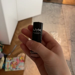 NYX läppstift med strassdetalj - Snyggt läppstift från NYX i svart hylsa med silverfärgade strasstenar runt botten. Färgen på stiftet ser ut att vara ljusrosa, perfekt för en fräsch look. Hylsan är stilren och modern, och materialet är plast med transparent botten.