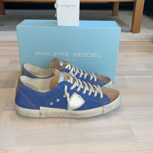 Blå Philippe Model sneakers i mocka - Snygga sneakers från Philippe Model i blått och brunt med vita detaljer. Skorna är köpta ifrån merchsweden för ett års sedan cirka och de har använts en gång men var lite för små så trotsade på om jag skulle behålla så blev att ja gjorde de men aldrig kommit till användning. Box och allt finns med! Köpta för 2799! Pris kan diskuteras