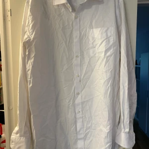 Vit klassisk skjorta från Dressmann strl: 2XL - Vit långärmad skjorta från Dressmann i storlek 2XL. Skjortan har klassisk krage, bröstficka och knäppning framtill. Tillverkad i bomull för en skön och luftig känsla. Perfekt för dig som gillar en stilren och enkel look.