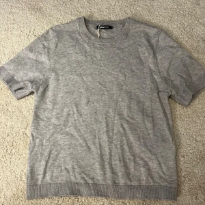 Grå stickad kortärmad tröja Gina Tricot - En enkel och stilren grå stickad tröja från Gina Tricot med korta ärmar och rund hals. Perfekt för dig som gillar en clean look och matrial. Verkligen aldrig använd och i superskick. Perfekt nu till hösten och skolan. 