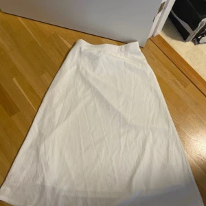 Vit långkjol  - Säljer en enkel och stilren vit långkjol i mjukt bomullstyg. Kjolen har en rak och klassisk form med resår i midjan för skön passform. Perfekt att matcha med sneakers eller sandaler för en chill look.