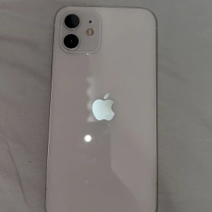 iPhone 12 - Snygg iPhone 12 i vitt med dubbla kameror och stilren design. Baksidan ser ut att vara i gott skick med endast mindre ytliga repor. Perfekt för dig som vill ha en pålitlig och modern smartphone från Apple. 94% batteri hälsa, tillkommer utan box och kvitto