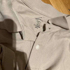 Beige pikétröja i bomull, storlek L - Snygg beige pikétröja från H&M i storlek L. Klassisk krage, korta ärmar och två knappar framtill. Tillverkad i mjuk bomull som är skön mot huden. Perfekt för dig som gillar enkel och stilren look.