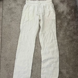 Vita  linnebyxor med snörning - Snygga vita linnebyxor med elastisk midja och grov snörning framtill. Byxorna har raka ben och två stora fickor framtill. Perfekta för en chill och avslappnad stil under varmare dagar.