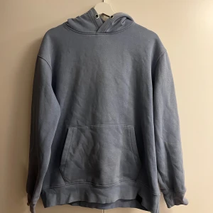 Ljusblå hoodie från Pull&Bear - Säljer en ljusblå hoodie från Pull&Bear i storlek M. Tröjan har en klassisk huva med snörning och en stor magficka framtill. Materialet är mjukt och känns skönt mot huden, perfekt för chill dagar. Passformen är loose och ärmarna är långärmade.