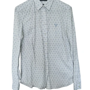 Vit mönstrad skjorta från GANT - Vit skjorta från GANT med diskret blått geometriskt mönster över hela tyget. Klassisk krage, långa ärmar och knäppning framtill. Tillverkad i mjuk bomull som känns skön mot huden. Perfekt för dig som gillar stilrena detaljer och snygg passform.