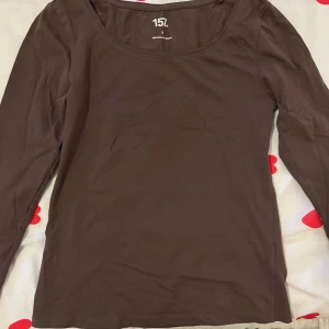 Brun långärmad topp från 157 - En basic brun långärmad topp från 157 i mjuk bomullsblandning med stretch. Rund halsringning och figurnära passform, perfekt att styla med jeans eller kjol. Materialet är 95% bomull och 5% elastan för extra komfort.