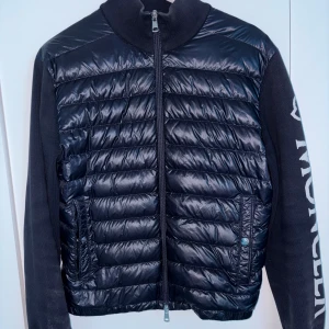 Mörk blå Moncler Cardigan  - Snygg Mörkblå Jacka från Moncler med quiltad framsida och mjuka ärmar. Jackan har dragkedja framtill, ståkrage och Moncler-logga tryckt längs ena ärmen. Perfekt för dig som vill ha en sportig och stilren look.