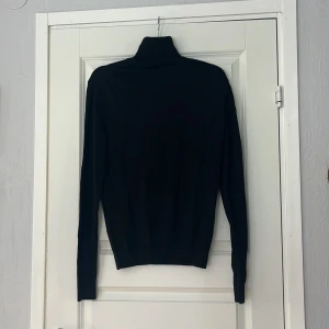 Svart polotröja från Conwell - Svart polotröja från Conwell i klassisk modell med lång ärm och hög krage. Tröjan är stickad.