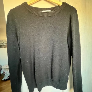 Svart stickad tröja från VILA - En enkel svart stickad tröja från VILA i storlek XS. Tröjan har rund halsringning och långa ärmar med ribbade muddar vid hals och nederkant. Perfekt för dig som gillar en clean och klassisk look.