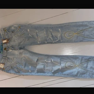 Ljusblå slitna jeans med broderier - Unika ljusblå jeans med coola detaljer! Inte mina bilder!! Midjemått 37cm innerbenslängd 82!
