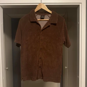 Oscar Jacobson skjorta - Brun skjorta i mjuk sammet med korta ärmar och klassisk krage. Skjortan har knappar framtill och en avslappnad passform, perfekt för en chill och stilren look.