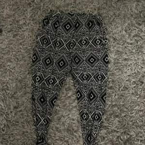 Svartvita mönstrade byxor Do Do - Säljer ett par svarta och vita byxor från Do Do i storlek XL/XXL. Byxorna har ett fett grafiskt mönster med rutor och detaljer, elastisk midja och smalare ben. Perfekta för dig som gillar att sticka ut med din stil.