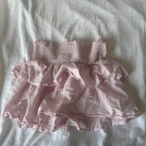 Rosa kjol/topp från Gina Young  - Supersöt ljusrosa kortkjol från Gina tricot  med bred smock i midjan och dubbla volanger. Kjolen är i tunn bomull och har en luftig känsla, perfekt för varma dagar. Enkel att matcha med en crop top eller t-shirt för en chill look. I storlek 158/164